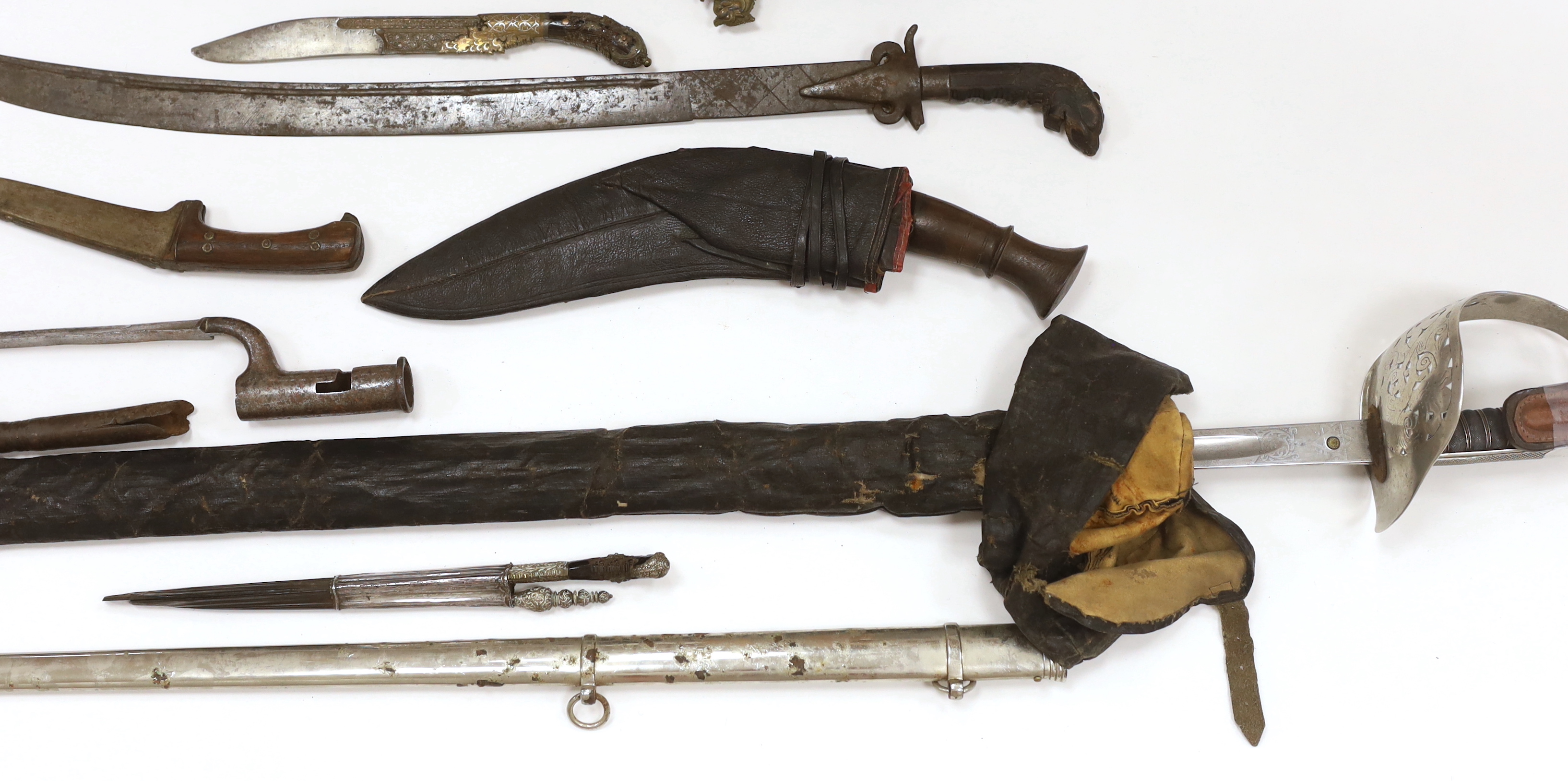 Two Sinhalese daggers and a kukri, a silver inlaid Kirichchiya dagger, together with another in a scabbard with a long pin, another dagger with a wooden handle, a head of a brass inlaid iron pole arm, a George V 1897 pat